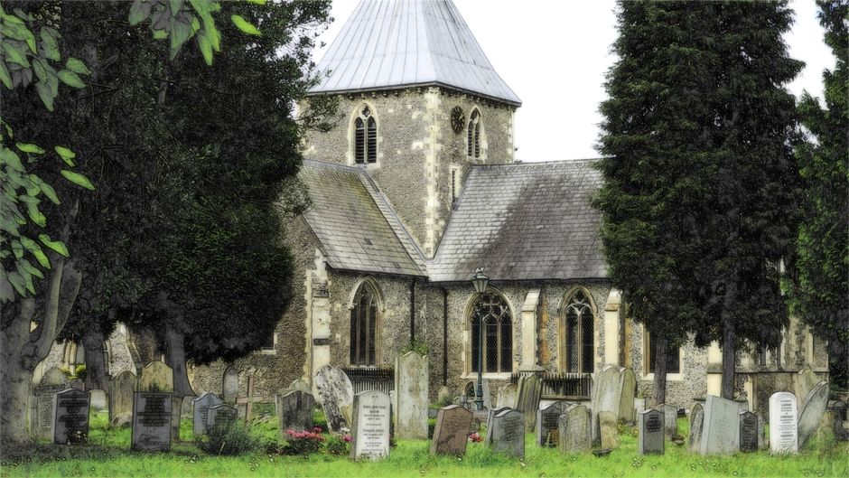 Photograph of a historic stone church with a tall, pointed spire and arched windows, situated on a grassy area with a gentle slope. The church has a red-tiled roof, and its exterior features weathered