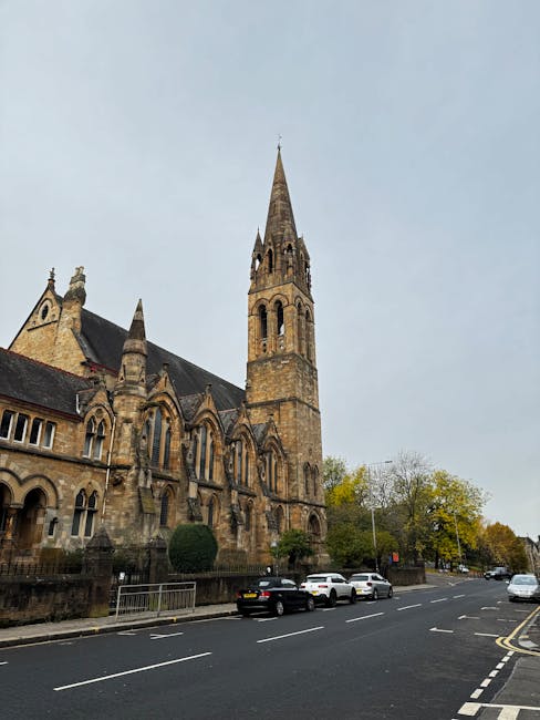 A person wearing a yellow t-shirt and blue jeans stands inside a room filled with packing and moving supplies. They are holding a clipboard in one hand and a black marker in the other, appearing to take notes or make a checklist. Surrounding them are several cardboard boxes, some open and others stacked, ready for packing and transportation. In the background, there are indoor plants with green and variegated leaves, positioned near a plain white wall and natural light illuminating the space. The person is currently engaged in planning or organizing belongings as part of a home relocation process. The scene captures the typical steps involved in packing, moving, and preparing items for transportation, consistent with services offered by Man with Van Church End in house removal and moving logistics.